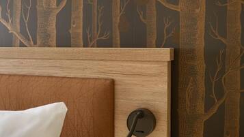 A hotel room with a wooden headboard, a bedside lamp, and a wall with a forest-themed wallpaper.