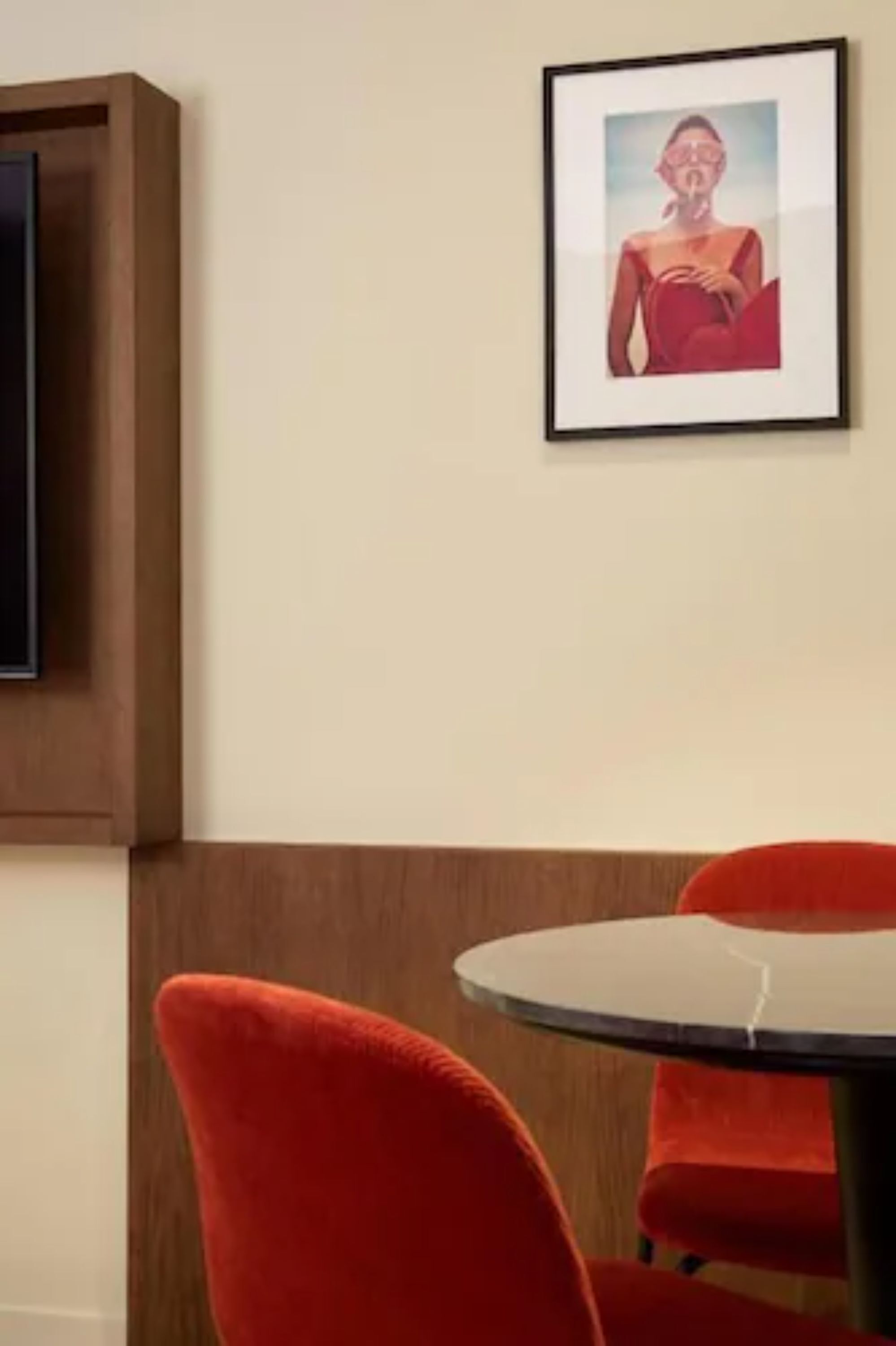 Una habitación con un armario de madera, un cuadro en la pared y una mesa redonda con sillas rojas.