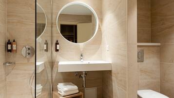 A modern bathroom with a glass-enclosed shower, a round mirror, a white sink, and a toilet.