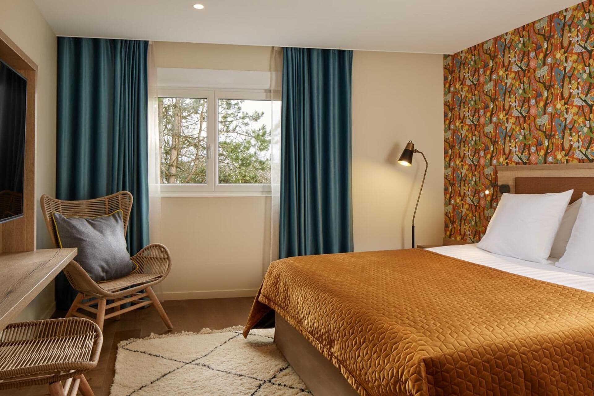 Quarto de hotel com cama, uma cadeira, escrivaninha e janela com cortinas.