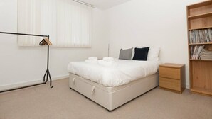 A minimalist bedroom with a bed, bedside table, and a bookshelf. - Centrally Located Spacious Flat (London)