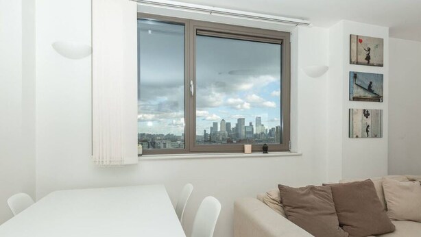 A modern living room with a dining area, a large window with a city view, and a wall with three framed artworks. - Centrally Located Spacious Flat (London)