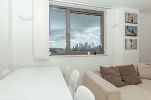 A modern living room with a dining area, a large window with a city view, and a wall with three framed artworks. - Centrally Located Spacious Flat (London)
