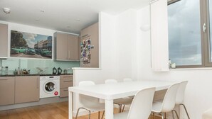A modern kitchen with a dining area, a washing machine, and a large window. - Centrally Located Spacious Flat (London)