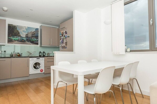 A modern kitchen with a dining area, a washing machine, and a large window. - Centrally Located Spacious Flat (London)