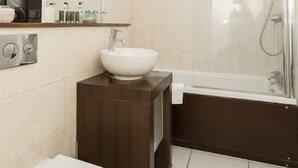 A modern bathroom with a white toilet, a wooden vanity with a white sink, and a glass-enclosed shower. - Centrally Located Spacious Flat (London)