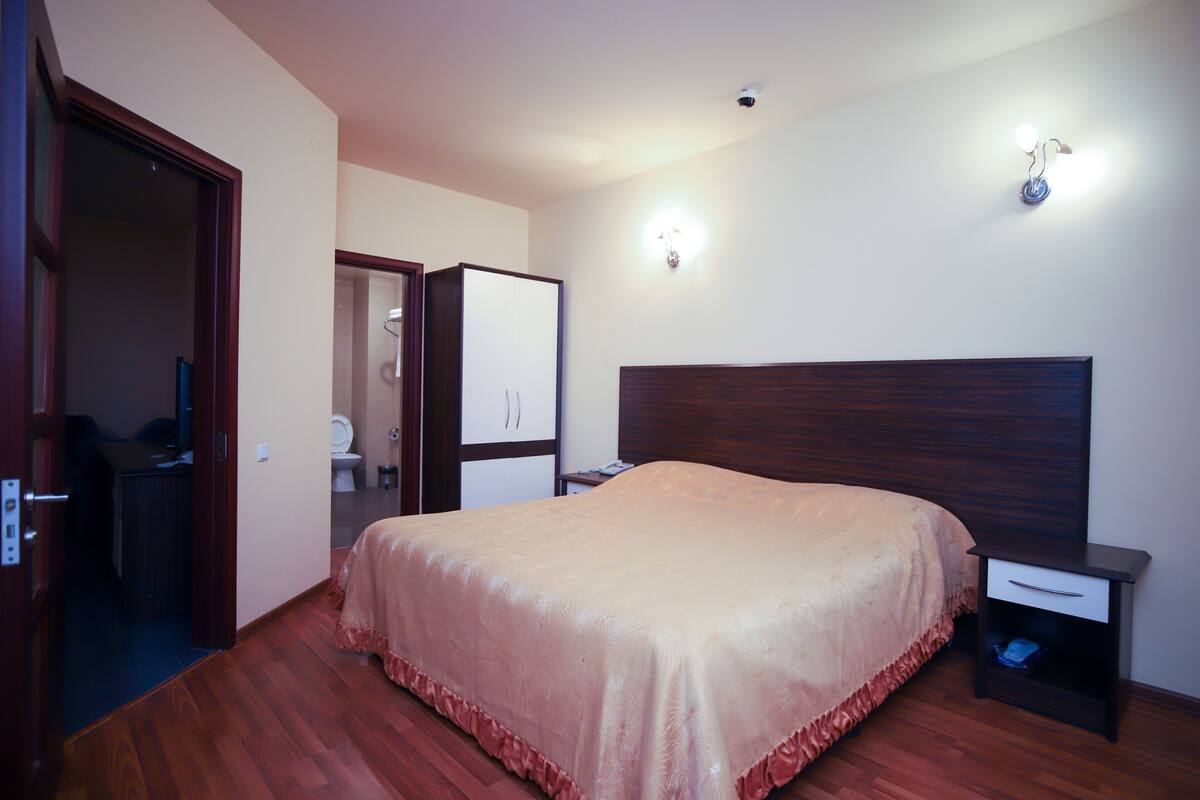 Een slaapkamer met een bed, nachtkastje, kast en een badkamer zichtbaar door een geopende deur.