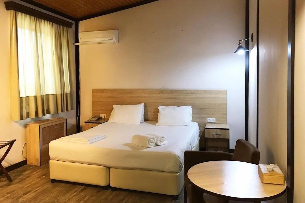 Een hotelkamer met een bed, nachtkastjes, een bureau, een stoel en een ronde tafel.