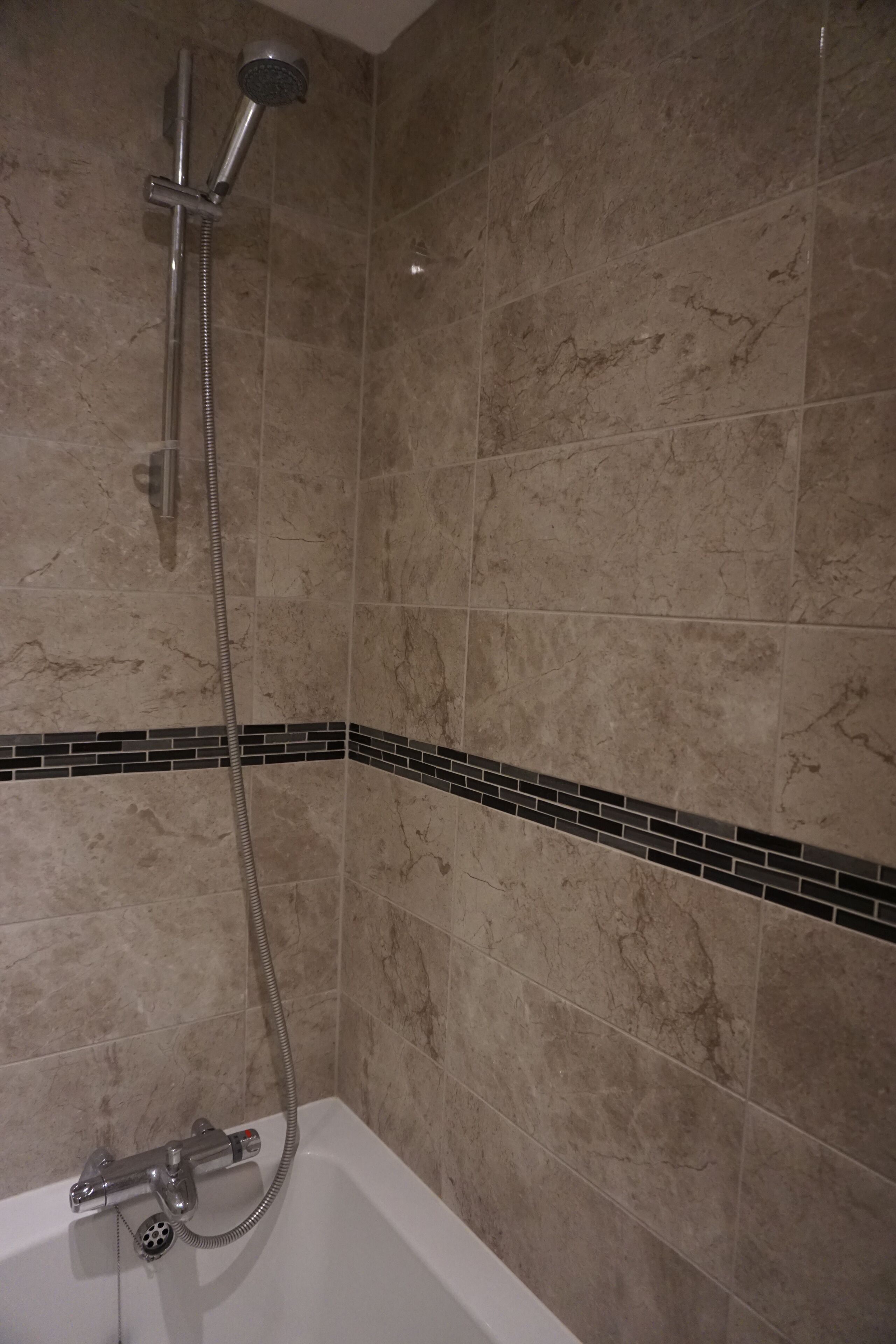 A bathroom with a bathtub, a showerhead, and a tiled wall.