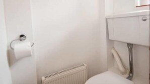 A small, white bathroom with a toilet, a radiator, and a trash bin. - Central London 2BR Apartment in Waterloo (London)