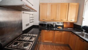A compact kitchen with wooden cabinets, a gas stove, a microwave, and a toaster. - Central London 2BR Apartment in Waterloo (London)