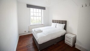 A bedroom with a large bed, a nightstand, a window, and a radiator. - Central London 2BR Apartment in Waterloo (London)