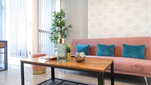 A modern living room with a wooden coffee table, a pink sofa with teal cushions, a potted plant, and a decorative bowl. - Tudors eSuites City Centre Apartment (Birmingham)