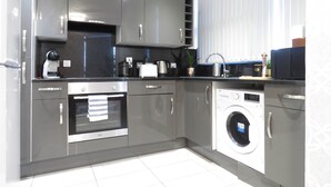 A modern kitchen with grey cabinetry, a built-in oven, a coffee maker, and a washing machine. - Tudors eSuites City Centre Apartment (Birmingham)
