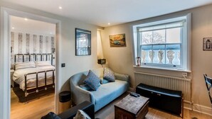 A compact living space with a bed, a sofa, a coffee table, and a radiator. - Lovely 1BR Flat Walk to Hyde Park (London)