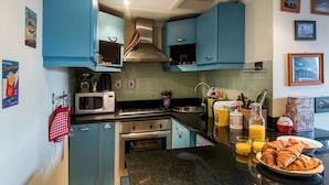 A kitchen with teal cabinets, a stainless steel range hood, a microwave, and a sink. There are various kitchen items on the counter, including a toaster, a kettle, and a glass of orange juice. - Lovely 1BR Flat Walk to Hyde Park (London)