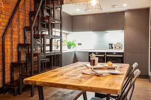 A modern kitchen with a wooden table, chairs, and a coffee machine. - Portland Street Apartments (Manchester)