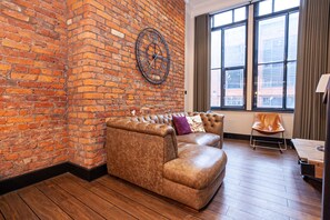 A room with a brick wall, a leather sofa, a clock, and a window with curtains. - Portland Street Apartments (Manchester)