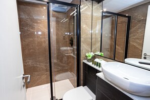 A modern bathroom with a glass-enclosed shower, a white sink, and a dark-toned vanity. - Portland Street Apartments (Manchester)