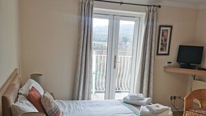 Een hotelkamer met een bed, een bureau, een stoel, een televisie en een raam met gordijnen.