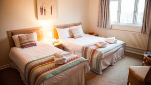 Een hotelkamer met twee bedden, elk voorzien van een gestreept dekbed en kussens, een nachtkastje met een lamp en een raam met gordijnen.