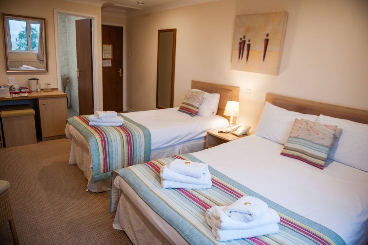 A hotel room with two beds, a desk, a chair, and a mirror.