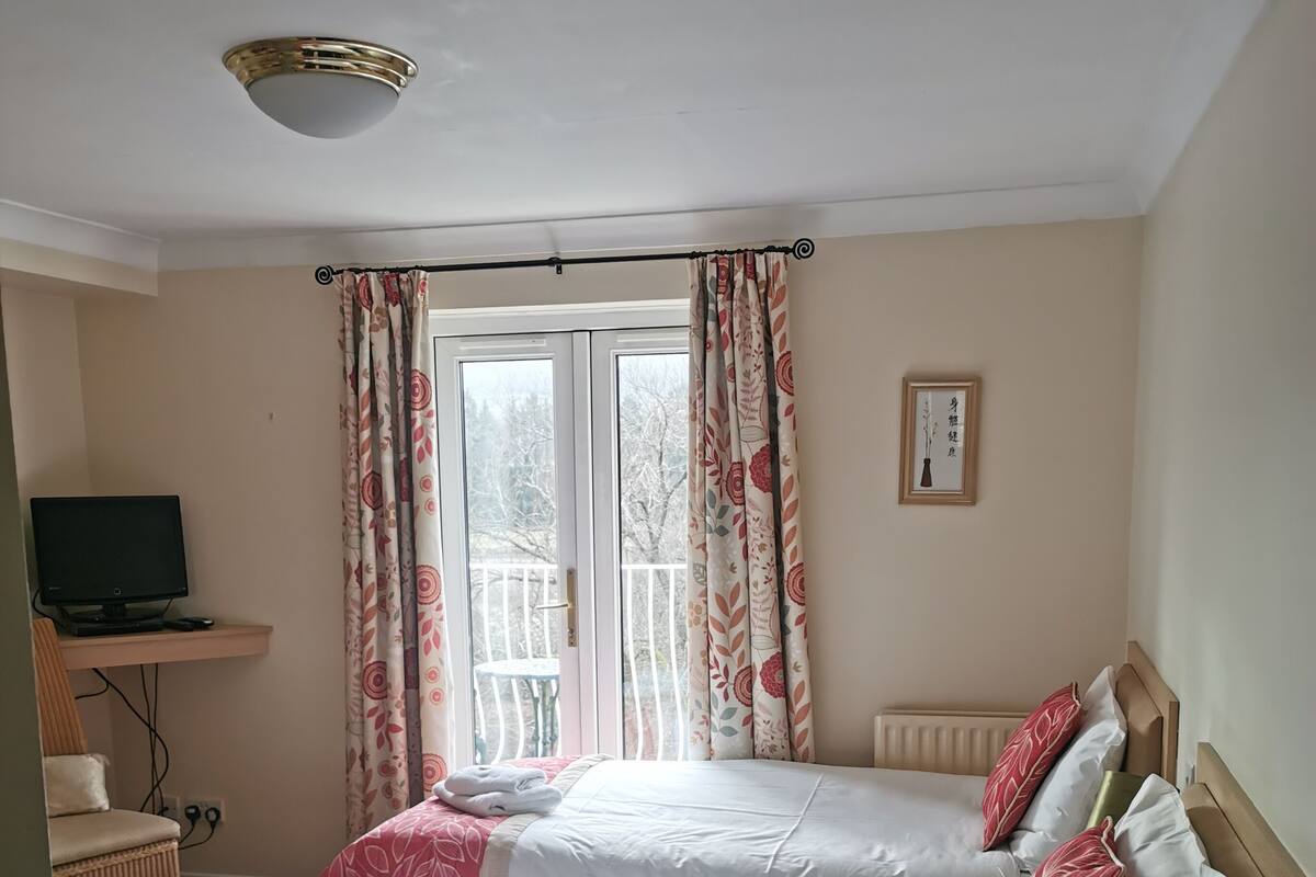 A hotel room with two beds, a TV, a desk, and a window with curtains.
