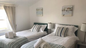 Habitación de hotel con dos camas, cada una con ropa blanca y colchas a rayas. Hay dos lámparas de noche, una ventana con cortinas y obras de arte en las paredes.