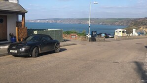 Un coche negro estacionado en una calle con vista al mar y colinas al fondo.