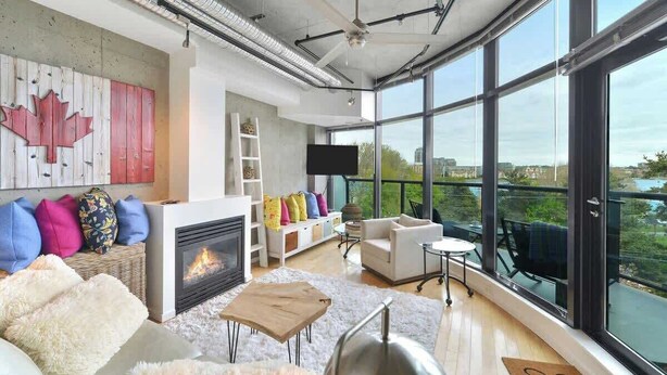 A modern living room with a fireplace, large windows, and a view of the city. - Harbourview Executive Condo (Victoria)