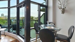 A modern dining area with a glass table and chairs, a mounted deer head on the wall, and large windows offering a city view. - Harbourview Executive Condo (Victoria)