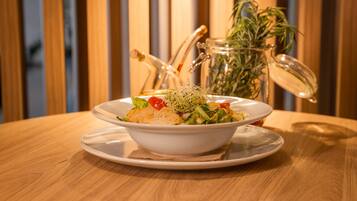 A white bowl of salad on a wooden table with a glass jar and a plant in the background.