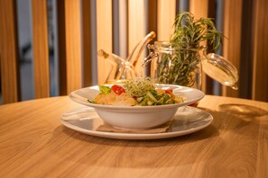 En vit skål med sallad står på ett träbord, och i bakgrunden syns en glasburk och en växt.