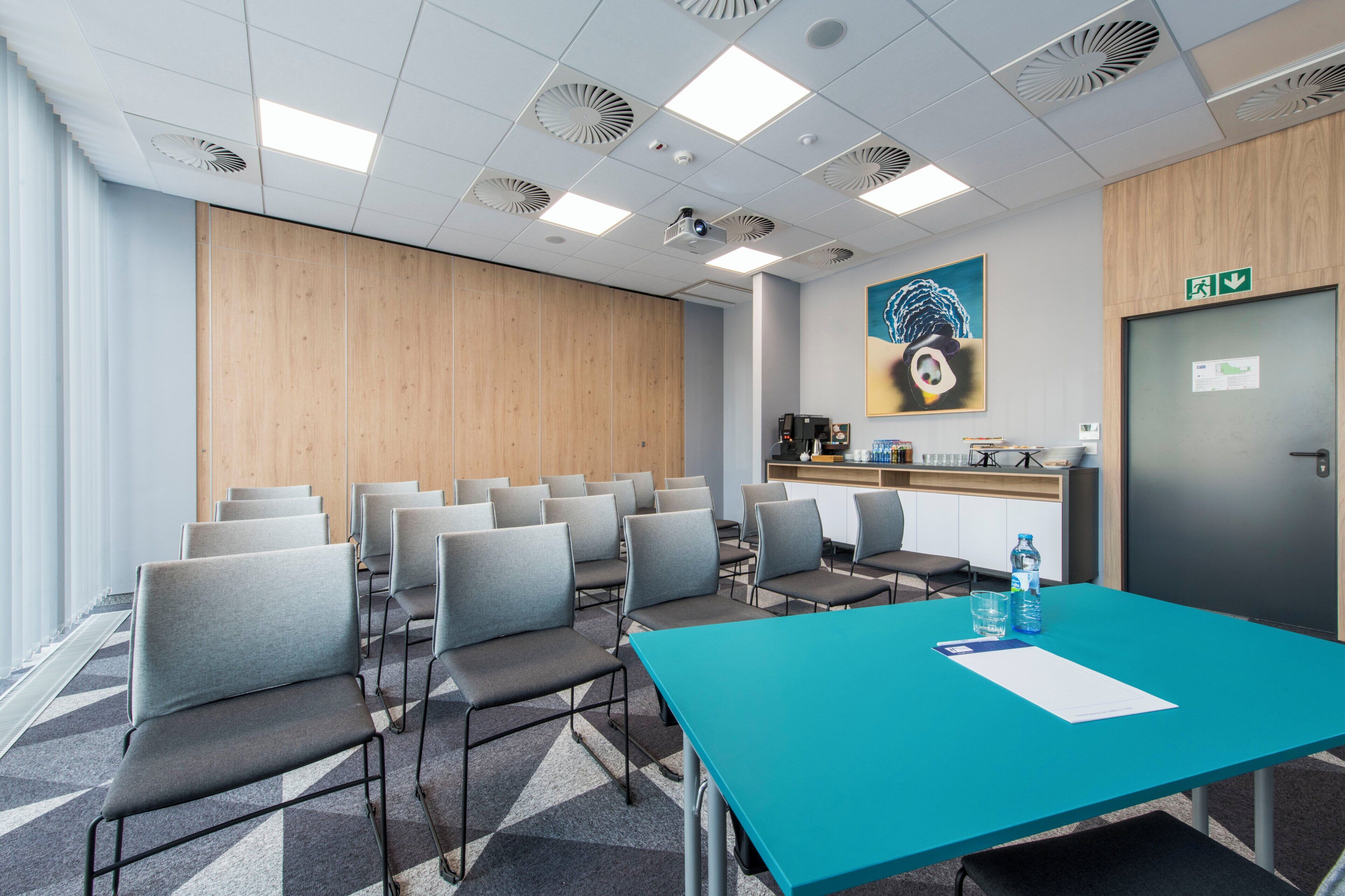 A conference room with a long table, chairs, a coffee station, and a painting on the wall.