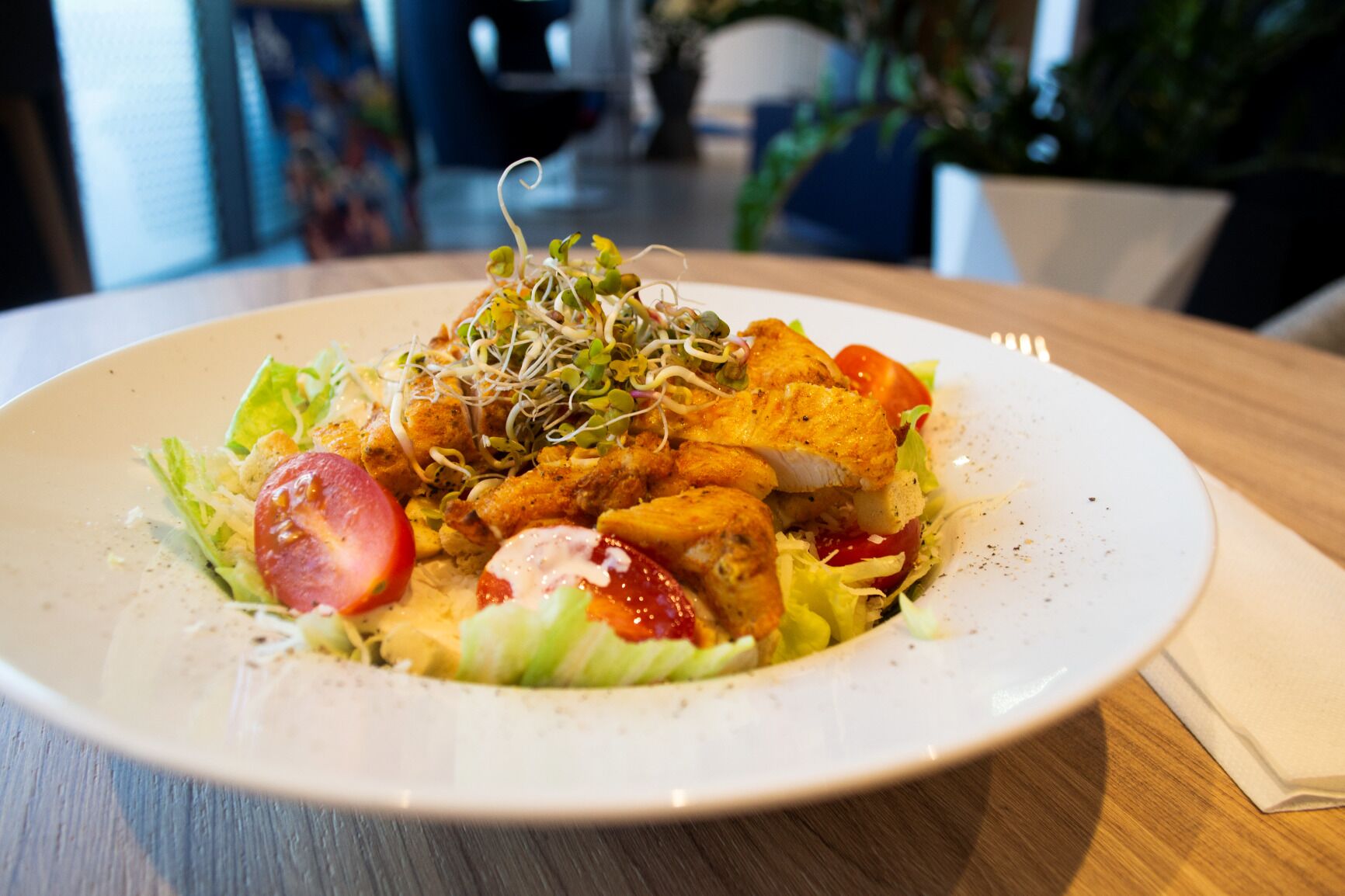 A plate of food with a salad, chicken, and sprouts on a wooden table.