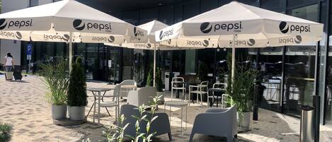 An outdoor seating area with Pepsi-branded umbrellas, potted plants, and a building with a Holiday Inn Express sign in the background.