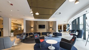 A modern lounge area with seating arrangements, a central table, and a television screen. - Holiday Inn Express Warsaw - Mokotow by IHG (Warsaw)