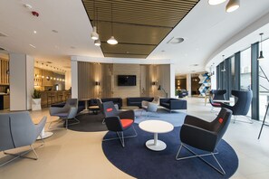 A modern lounge area with seating arrangements, a central table, and a television screen. - Holiday Inn Express Warsaw - Mokotow by IHG (Warsaw)