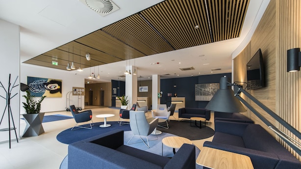 A modern hotel lobby with blue seating areas, a reception desk, and a large TV screen. - Holiday Inn Express Warsaw - Mokotow by IHG (Warsaw)