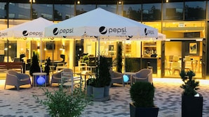 An outdoor seating area with Pepsi-branded umbrellas, potted plants, and a modern building facade. - Holiday Inn Express Warsaw - Mokotow by IHG (Warsaw)