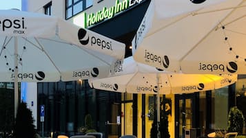 Outdoor seating with umbrellas branded with Pepsi Max, in front of a Holiday Inn Express building.