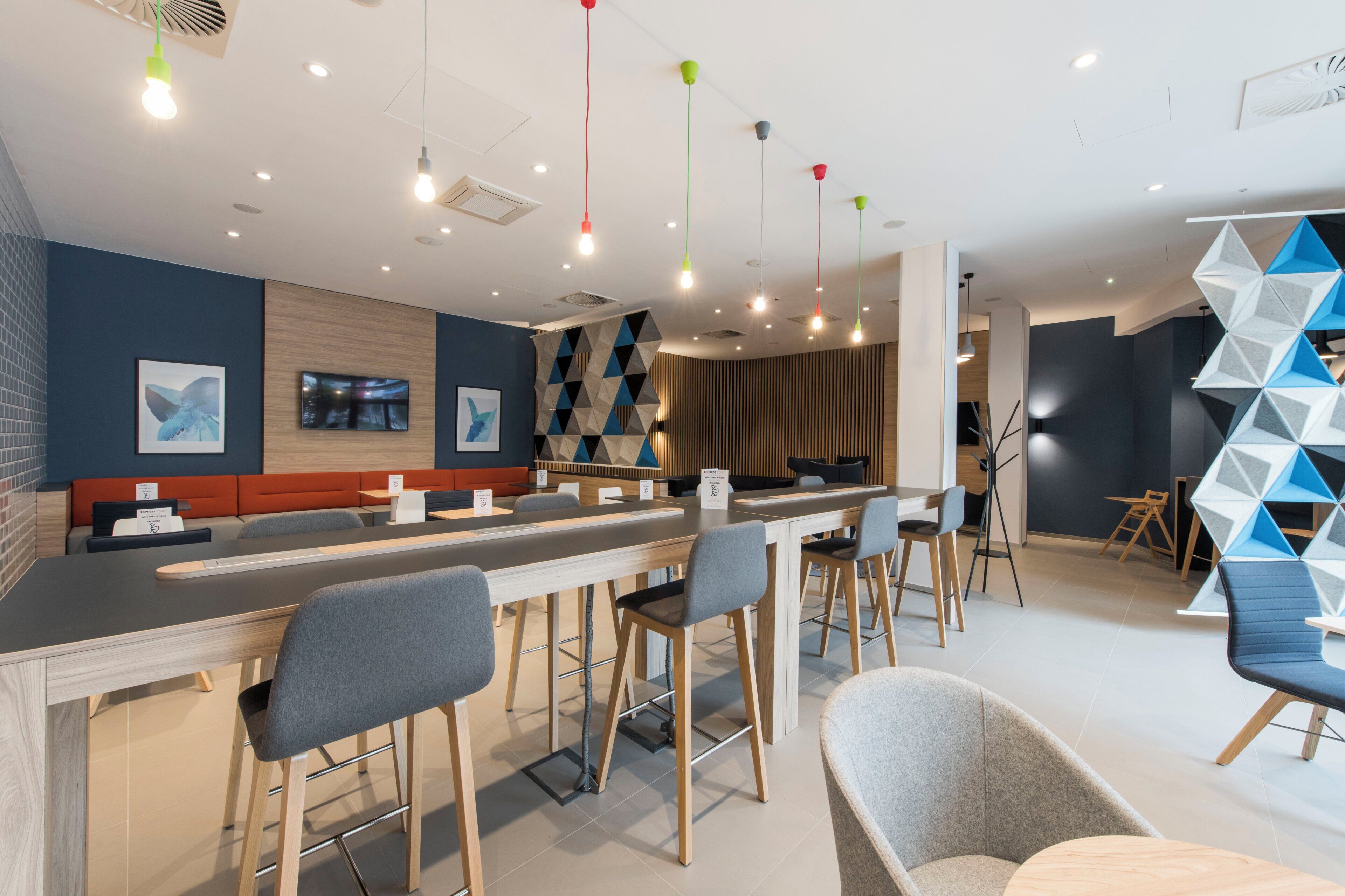 Un moderno bar con una barra alargada, taburetes y una zona de estar con un diseño geométrico en la pared.