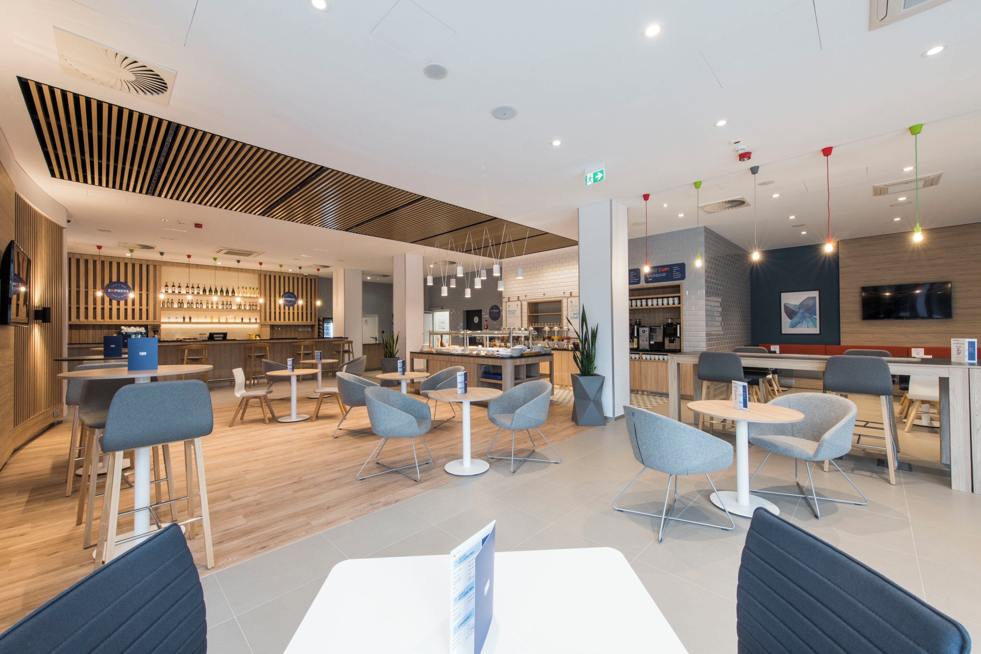 Un restaurante moderno con barra, asientos con taburetes y mesas, y una variedad de luminarias.