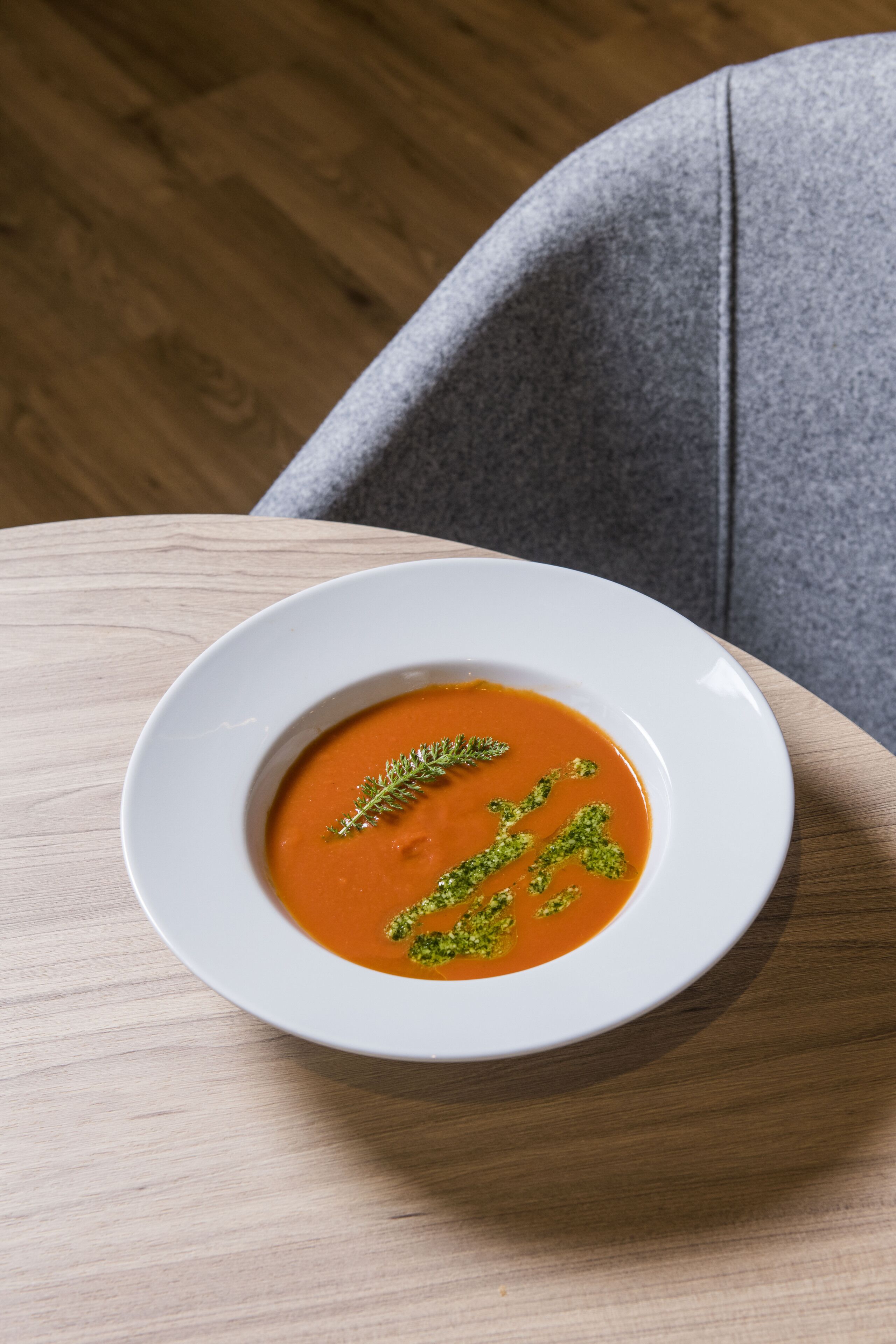 A bowl of soup on a wooden table with a grey chair in the background.