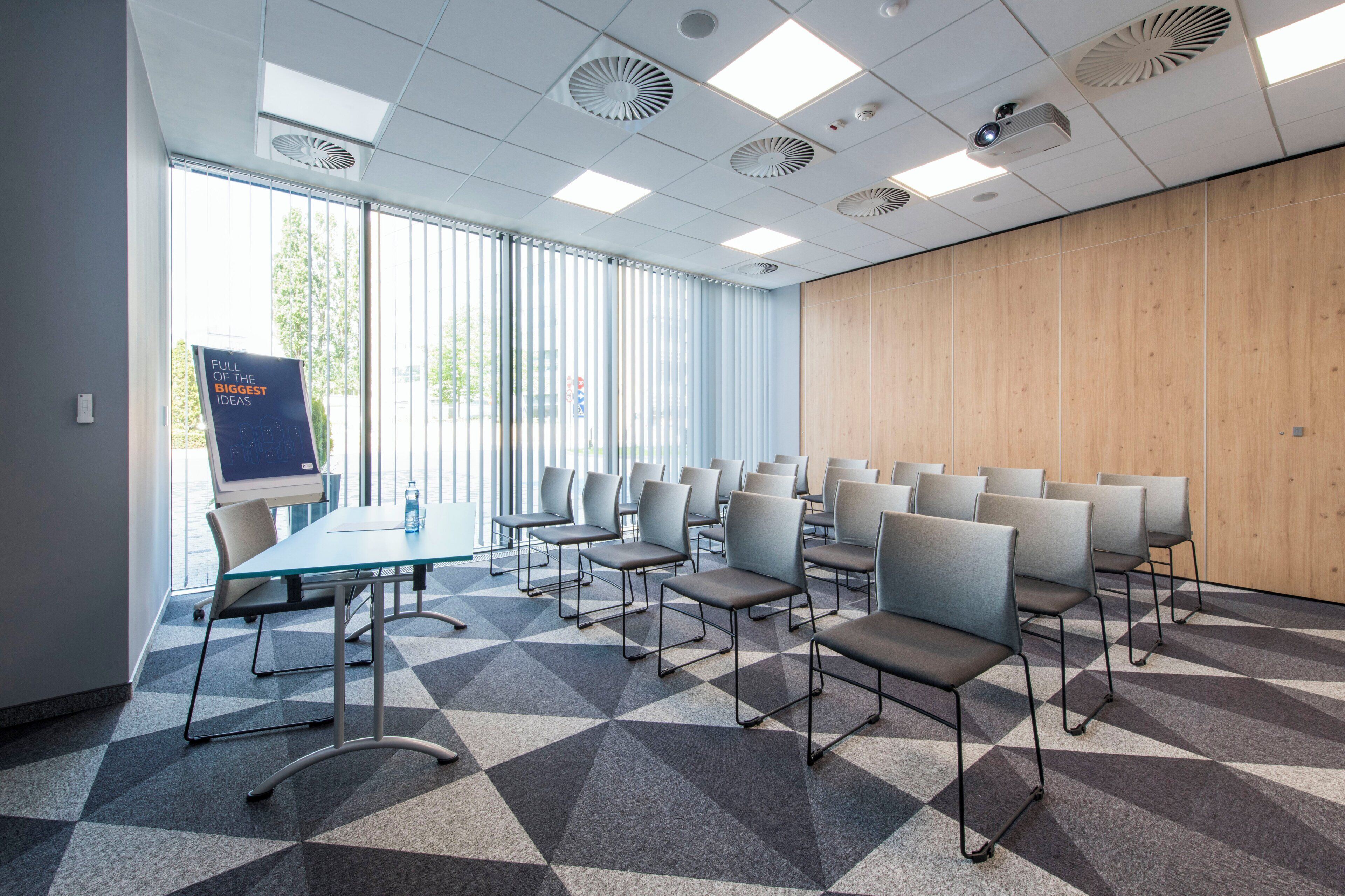 A conference room with a glass table, multiple chairs, a projector, and a large window with blinds.