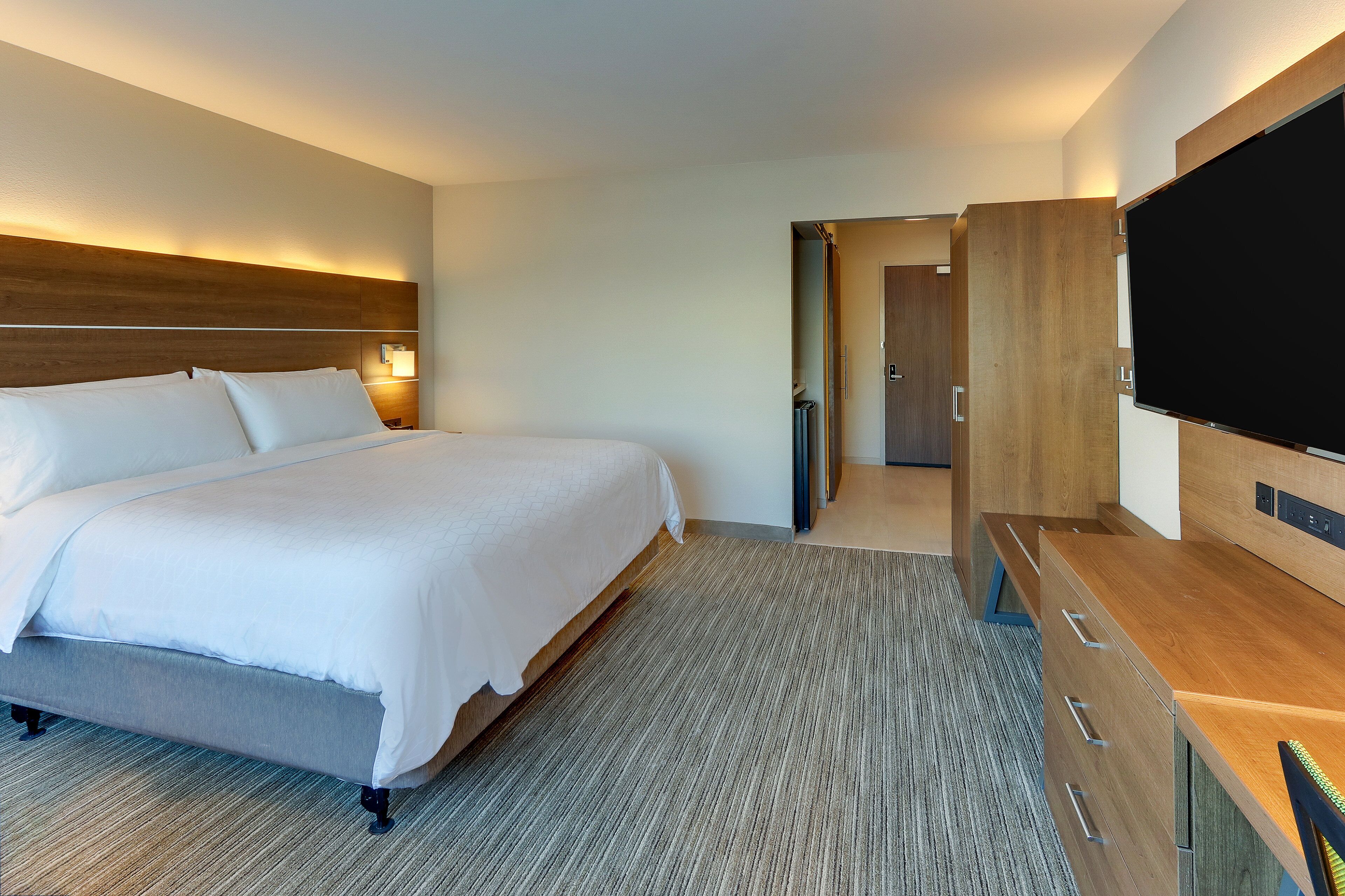 A hotel room with a large bed, a flat-screen TV, a wooden dresser, and a walk-in closet.