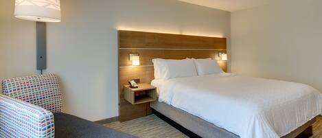 A hotel room with a bed, a chair, a nightstand, and a wall-mounted lamp.