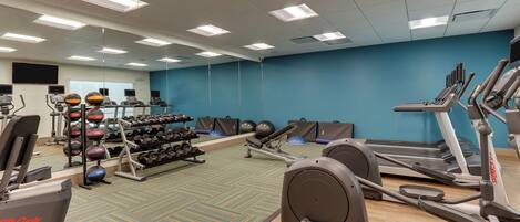 Une salle de sport équipée de tapis de course, de vélos elliptiques et de poids libres.
