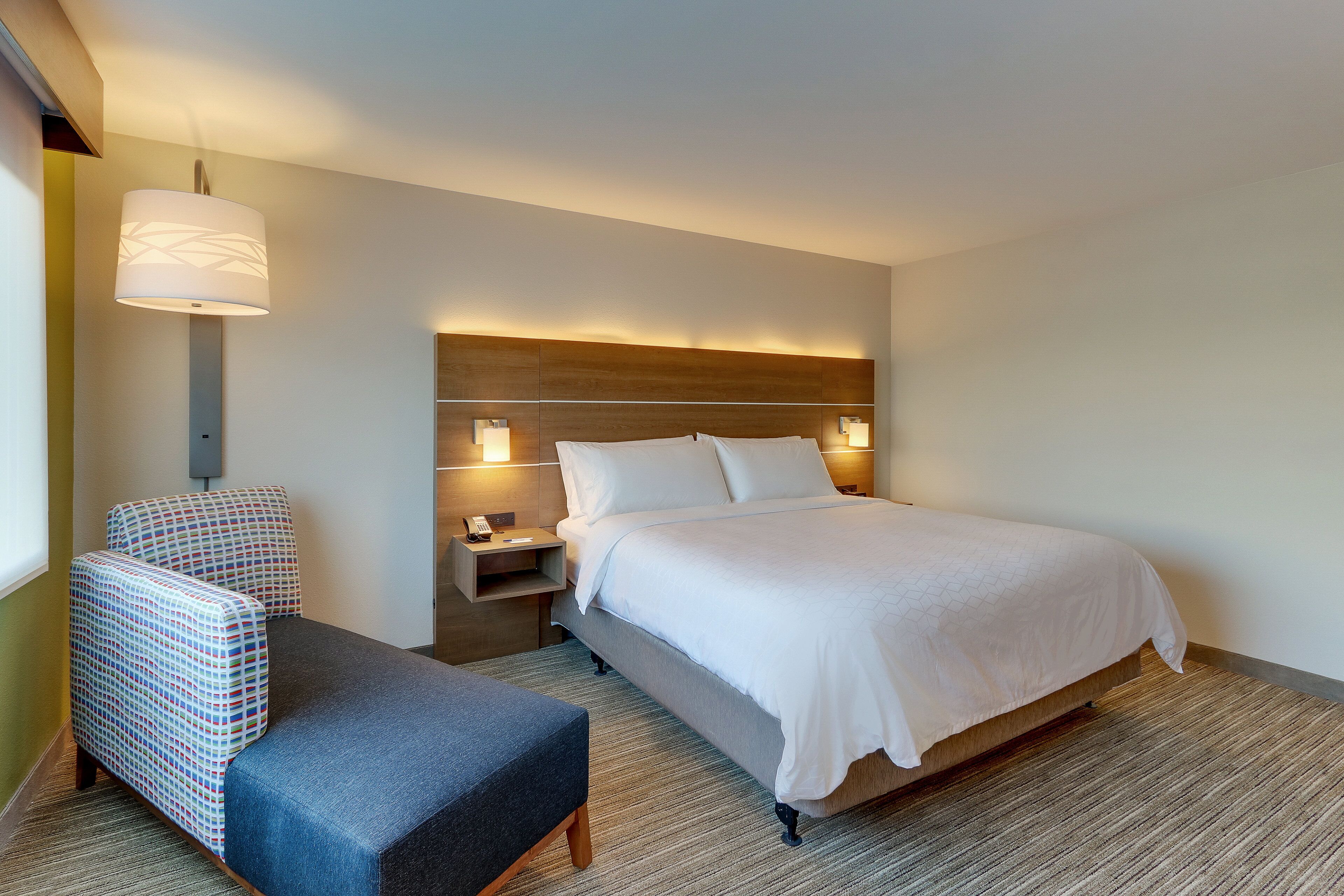 A hotel room with a bed, a chair, a nightstand, and a lamp.