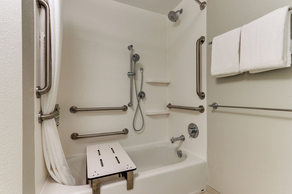 A bathroom with a bathtub, grab bars, a showerhead, and a towel rack.